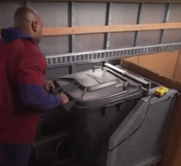 Man using cart tipper in the back of a truck into a large open box.